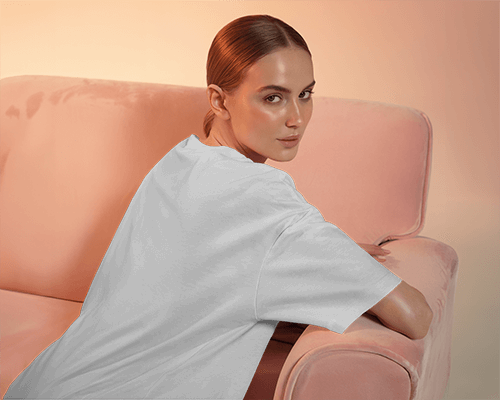 Back View T Shirt Mockup Female Model On Pink Sofa With Soft Warm Lighting And Casual Pose
