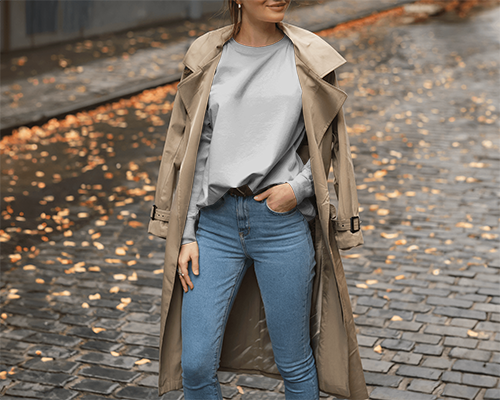 American Model T Shirt Mockup Female Standing On Cobbled Street Autumn Styling With Trench Coat Cozy And Chic Vibes
