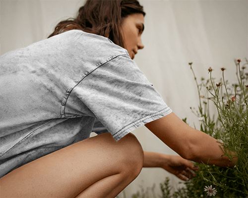Acid Wash Outdoor Garden T Shirt Mockup Female Model Kneeling Among Wildflowers In Natural Daylight Soft And Earthy Aesthetic 0770