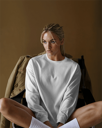 Moody Studio Blank Round Neck Long Sleeve T Shirt Mockup Women Model In White Tee Relaxed Pose Warm Neutral Background 0826