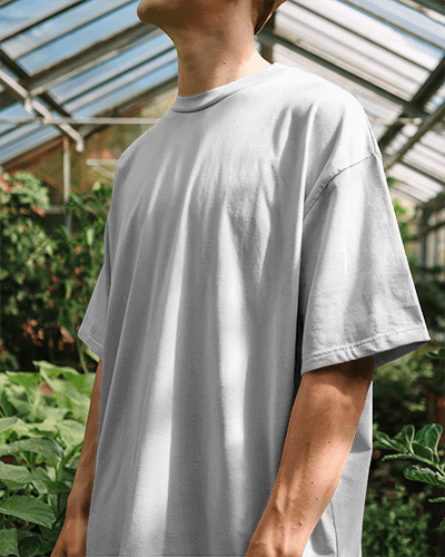 Sunlit Greenhouse Blank Round Neck T Shirt Mockup Man In Light Gray Oversized Tee Natural Light And Lush Greenery 0827