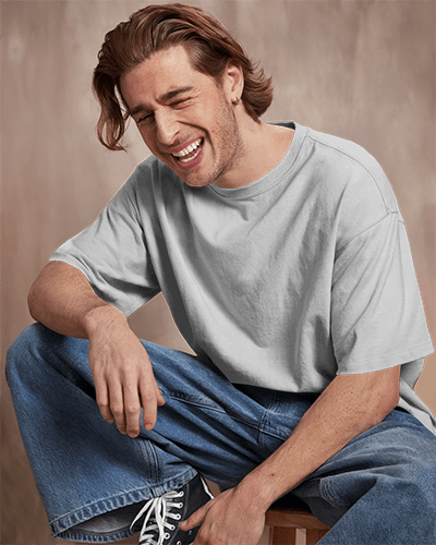 Studio Portrait Blank White Tshirt Mockup Smiling Male Model Sitting Casually In Loose Denim Soft Lighting Warm Backdrop Relaxed And Joyful Vibe 0893