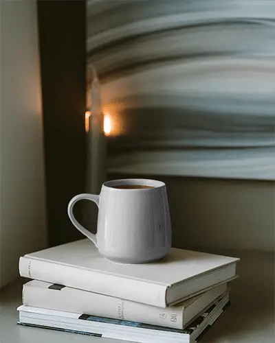ceramic-coffee-mug-on-stack-of-books-near-abstract-wall-art-and-candlelight-setting-for-relaxation