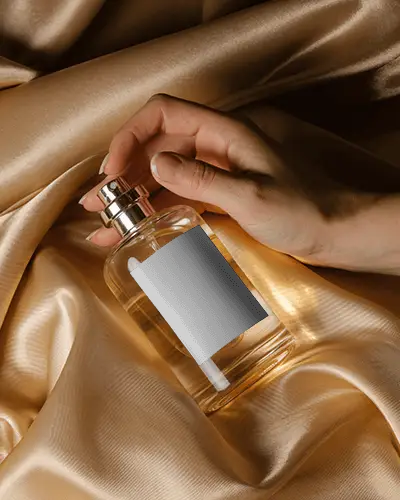 artistic-perfume-mockup-hand-gripping-clear-glass-bottle-on-luxury-golden-fabric-soft-lighting