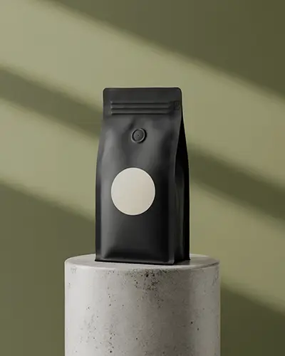 Matte Black Coffee Pouch Sticker Mockup On Round Pedestal With Soft Shadow And Green Background 0194