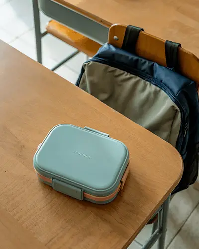 school-lunchbox-sticker-mockup-on-wooden-desk-with-backpack-in-background