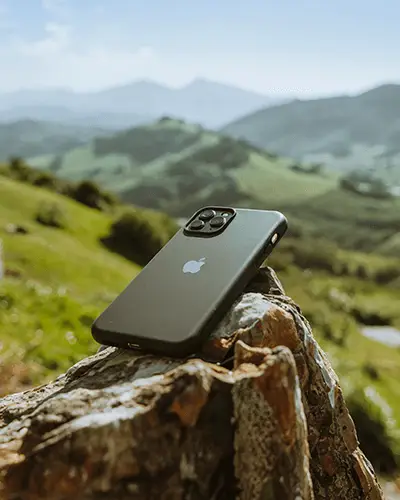 modern-phone-case-mockup-placed-on-rock-with-blurred-mountains-and-greenery-in-background