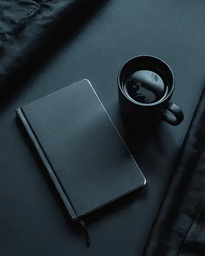 Minimalistic Black Notebook And Coffee Mug On Dark Textured Background Sticker Mockup
