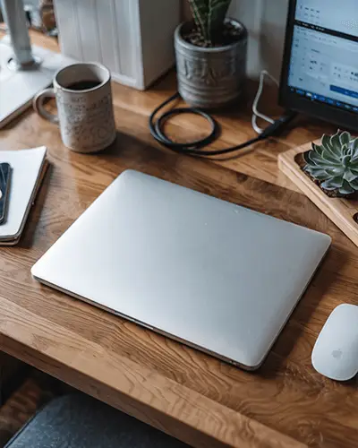 closed-modern-laptop-sticker-mockup-on-wooden-desk-with-coffee-plant-and-computer-accessories