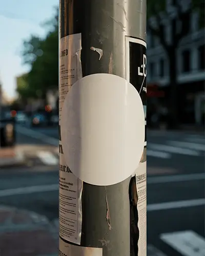 White Circular Sticker Mockup Attached To Street Pole With Cityscape Out Of Focus