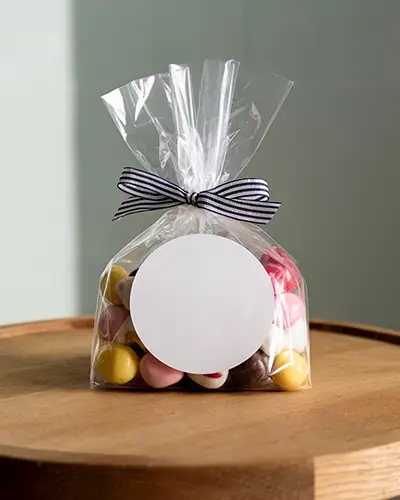 Blank Round Sticker Mockup On Transparent Bag Gift Packaging With Striped Ribbon Tie
