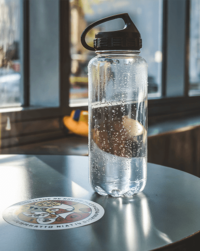 Modern Sticker Mockup On Metal Table Sunlit Café Setting With Water Bottle