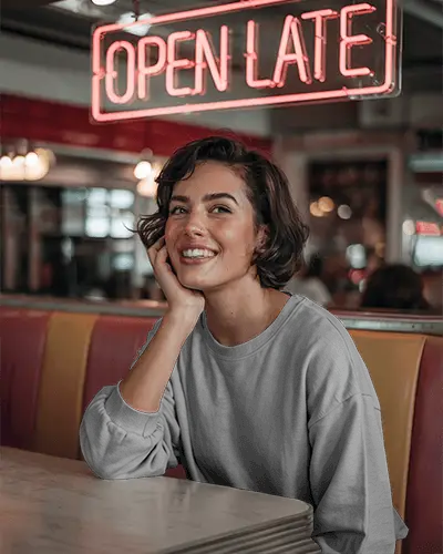Retro Diner Sweatshirt Mockup Smiling Female Model Sitting In Booth Under Open Late Neon Sign Vibrant And Nostalgic Vibes