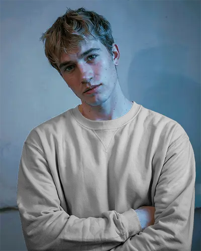 Moody Studio Sweatshirt Mockup Male Model Crossed Arms Cool Toned Lighting Blue Background Soft Shadows Artistic Expression Modern Grunge Style