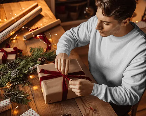 Christmas Sweatshirt Mockup Man Wrapping Gift On Wooden Table With Holiday Decor