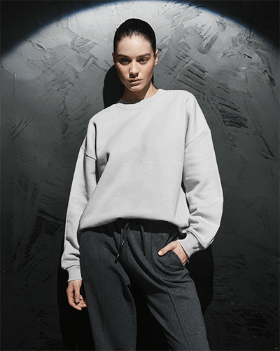 Textured Wall Sweatshirt Mockup Female Model Leaning In Soft Shadowed Lighting