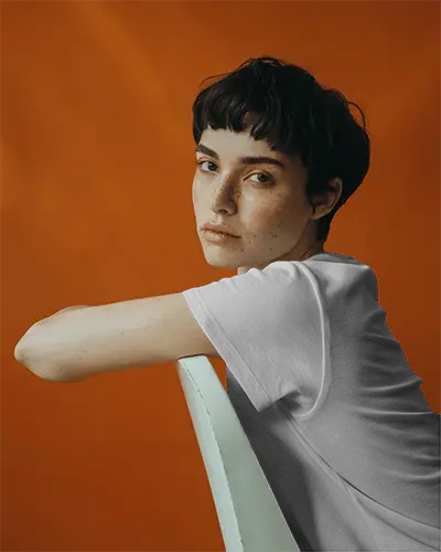 T Shirt Mockup Retro Inspired Orange Wall Setting Female Model With Neutral Expression And Freckles