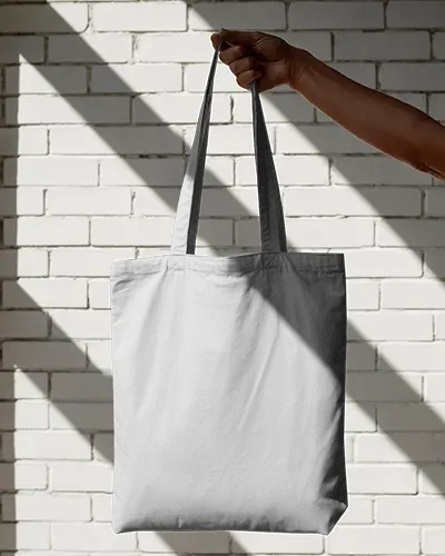 Hand Holding Tote Bag Mockup In Sunlit White Brick Wall Background Contrasting Light And Shadows