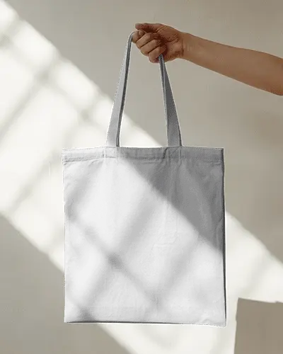hand-holding-tote-bag-mockup-against-bright-wall-with-sunlight-shadows