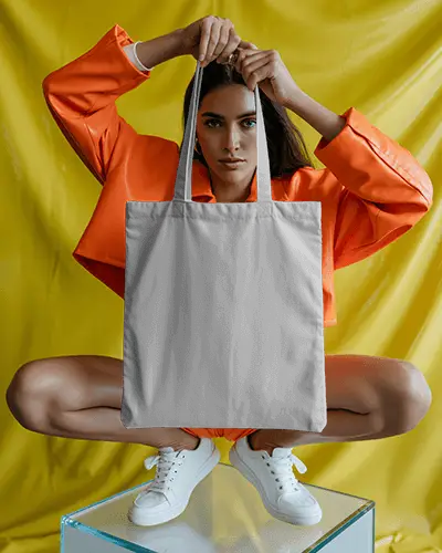 Bold Fashion Tote Bag Mockup Model Posing Against Yellow Backdrop In Orange Jacket Studio Vibe