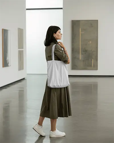 Casual Elegant Woman Showcasing Soft Fabric Tote Bag Mockup In Contemporary Art Gallery Space