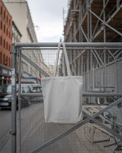 Urban Street Scene Tote Bag Mockup Hanging On Metal Fence For Design Presentation