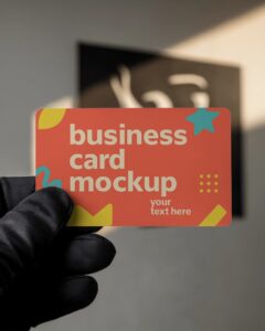 hand holding rounded corner business card mockup in black glove with moder blurred background and soft light

